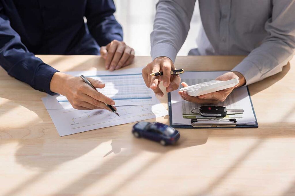 A person reviews insurance documents and medical bills at a kitchen table with a calculator and paperwork.